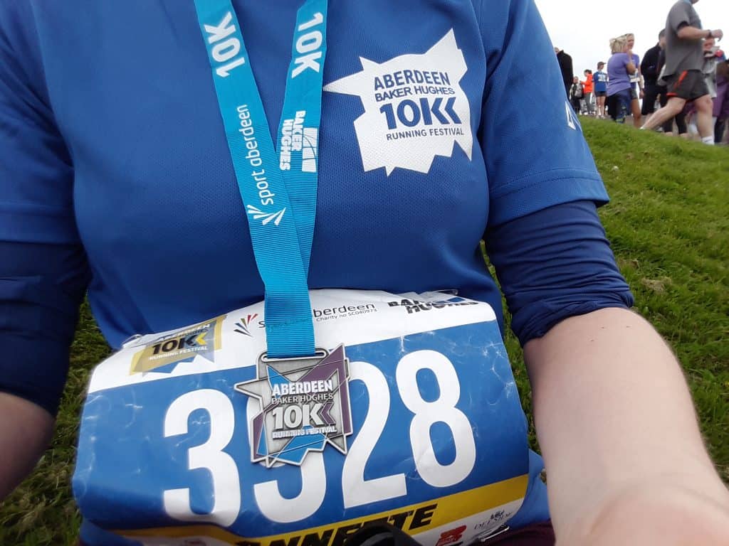 Baker Hughes 10K race t-shirt, medal and bib with people in the background.
